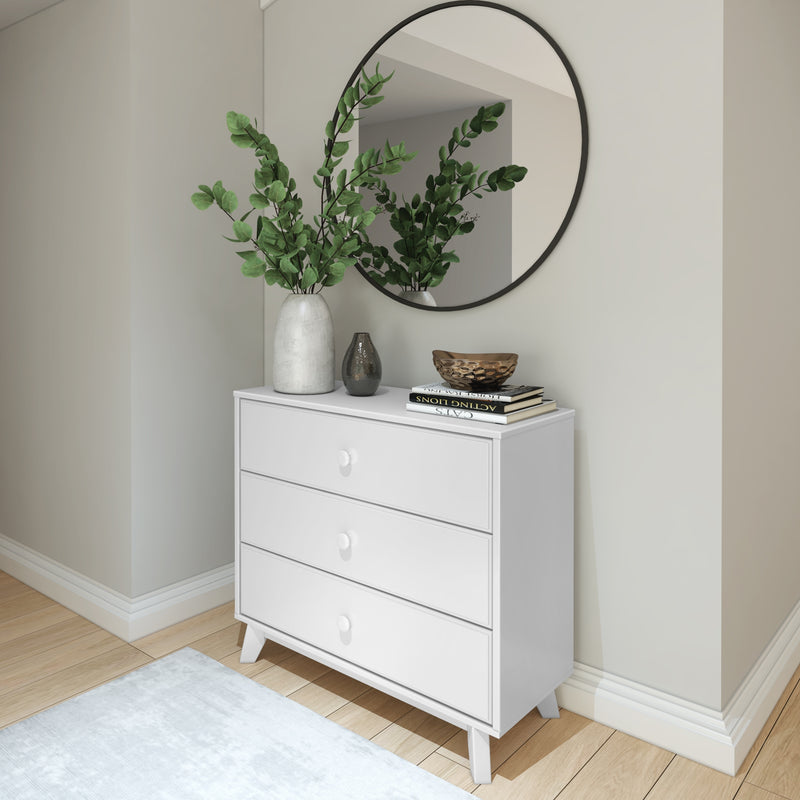 Modern white dresser with drawers and decorative items including a round mirror, vase with green leaves, and books in minimalist interior design.