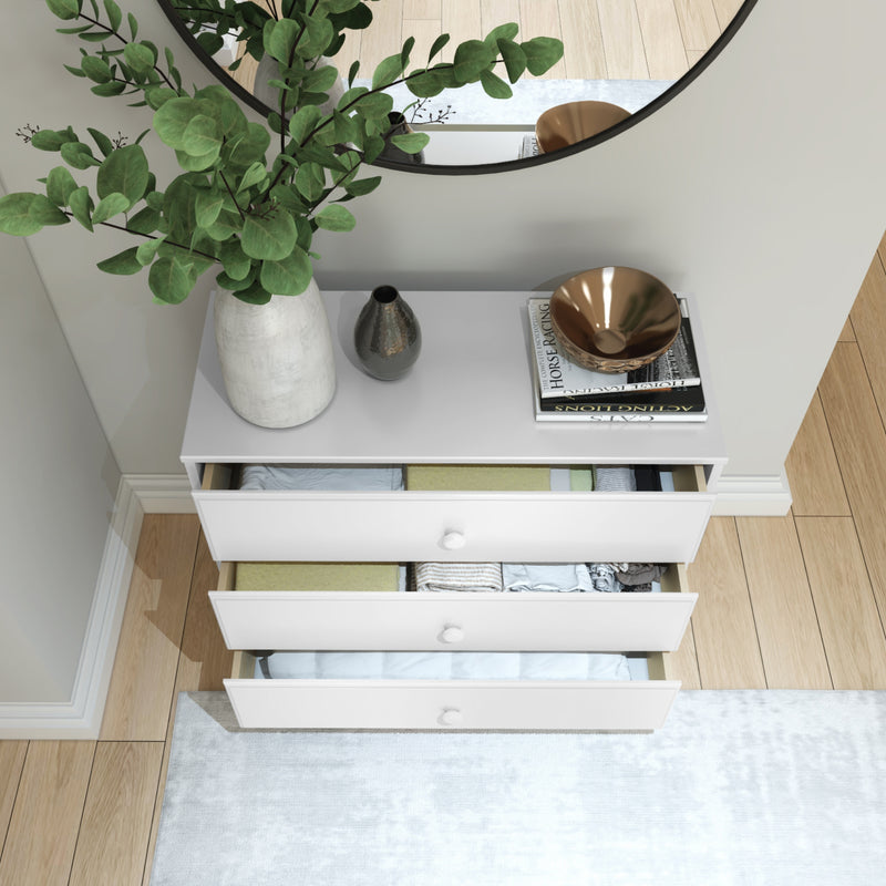 Modern white dresser with open drawers and decorative items, including a green plant, placed in a stylish bedroom setting with wooden floors.