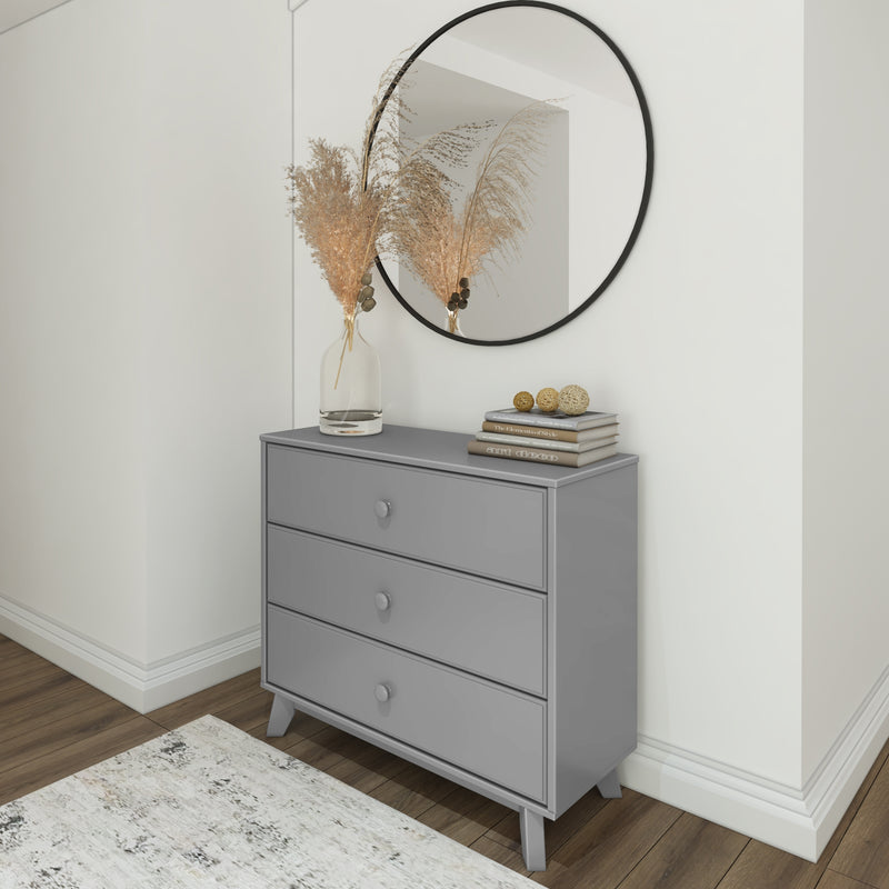 Gray dresser with three drawers, decorated with a vase of dried pampas grass, books, and round decorations, positioned next to a circular wall mirror in a modern living space.