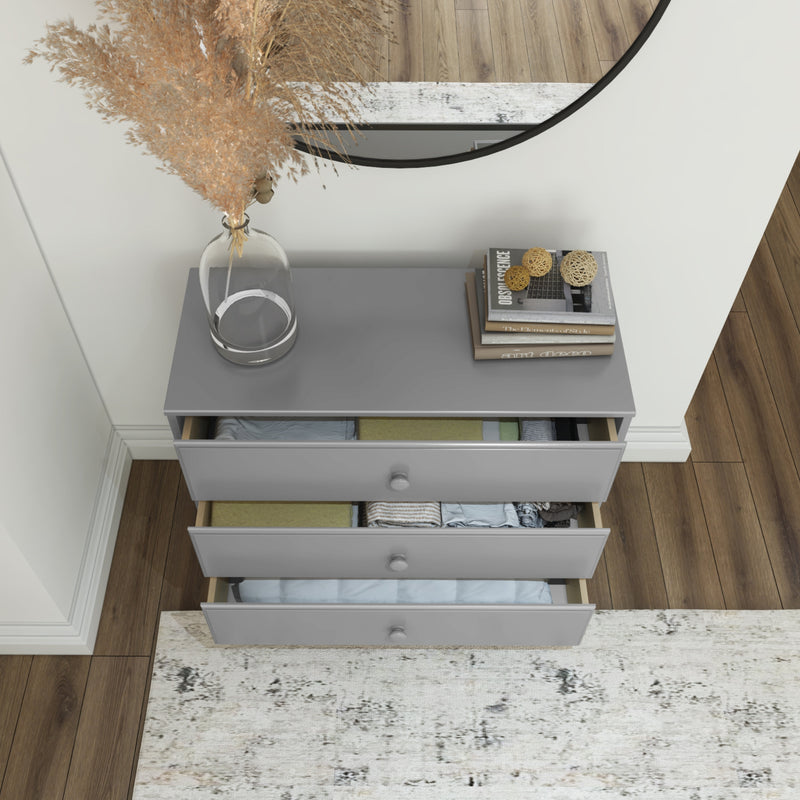 Gray dresser with open drawers filled with clothes, round mirror, books, and decorative vase in modern bedroom.