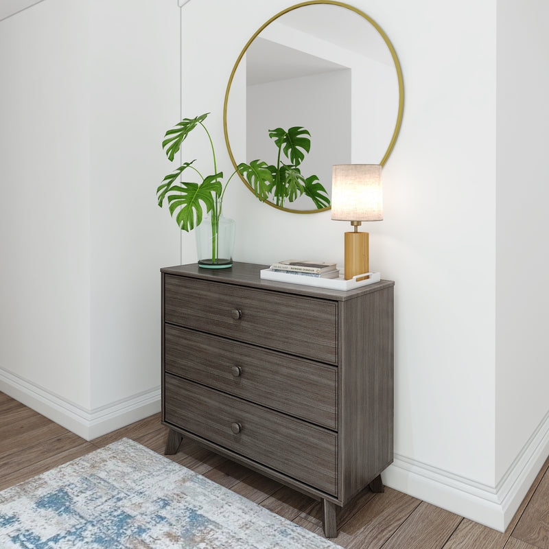 Modern wooden dresser with a round mirror, potted plant, stack of books, and table lamp in a stylish living room.