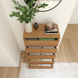 Wooden chest of drawers with decorative vases and books on a hardwood floor in a modern interior setting.
