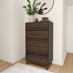 Tall wooden dresser with four drawers in modern interior, featuring decorative plants and rustic decor items on top.