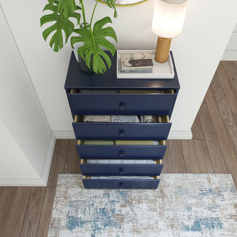 Navy blue dresser with open drawers showcasing neatly folded clothes, topped with a potted plant, books, and a lamp, on hardwood floor.