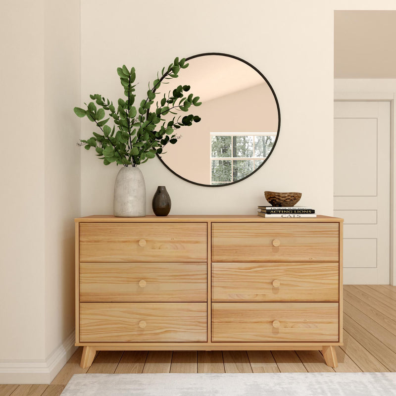 Modern minimalist bedroom with wooden dresser, round mirror, and decorative plants.