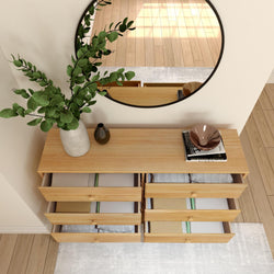 Modern wooden dresser with six open drawers, decorative vase with green leaves, and round mirror reflects a bright room.