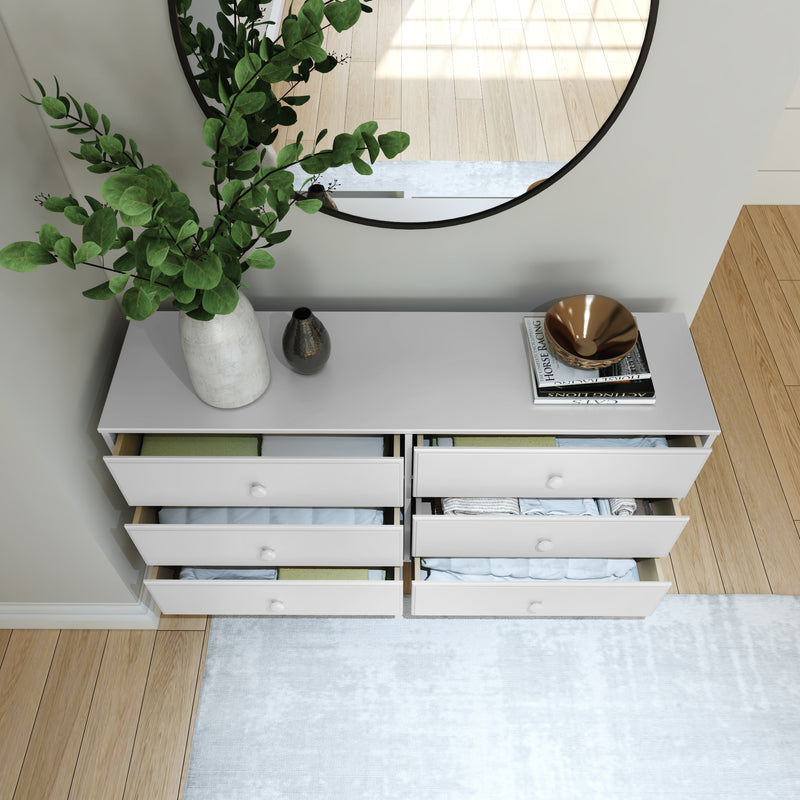 Modern white dresser with open drawers, green vase, and decorative items, placed on a light wood floor with a round wall mirror.