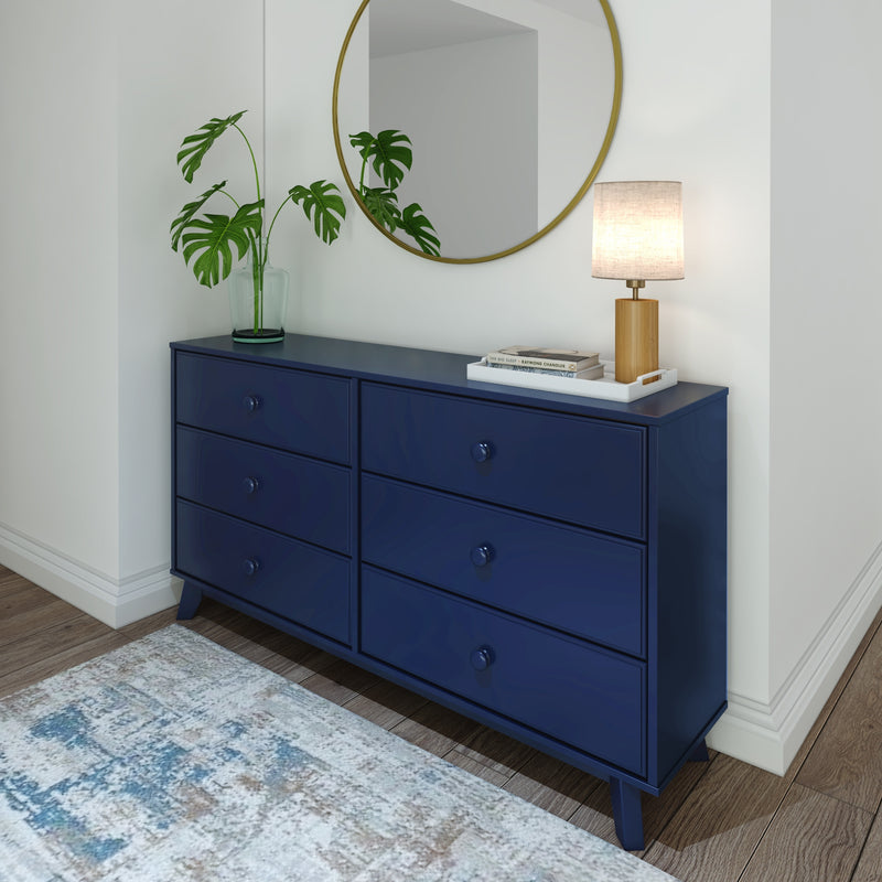 Blue dresser with six drawers, round mirror, and decorative items including a plant and lamp, enhancing modern home interior design.
