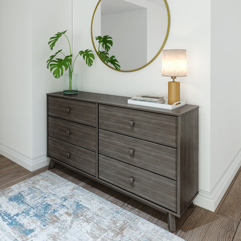 Modern bedroom dresser with six drawers, featuring a round mirror, decorative plant, and lamp, set on elegant wooden flooring.