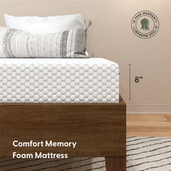 8-inch Comfort memory foam mattress with quilted white cover and textured decorative pillow on a wooden platform bed, 10-year warranty badge