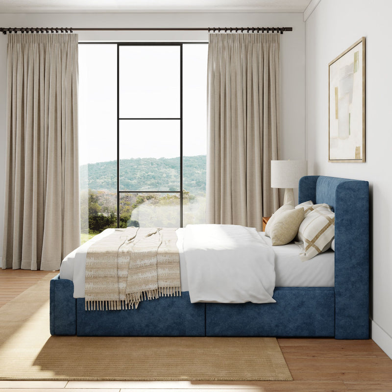 Contemporary bedroom with blue upholstered bed frame, beige curtains, large window with scenic view, and cozy neutral accents.