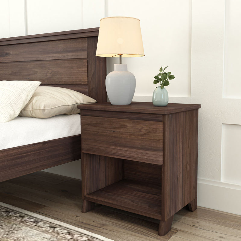 Wooden nightstand with lamp and plant next to a bed in a modern bedroom.