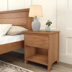 Wooden bedside table with drawer featuring a modern lamp and small plant, next to a bed with a beige pillow.
