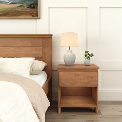 Wooden nightstand with a modern table lamp beside a bed in a cozy minimalist bedroom.