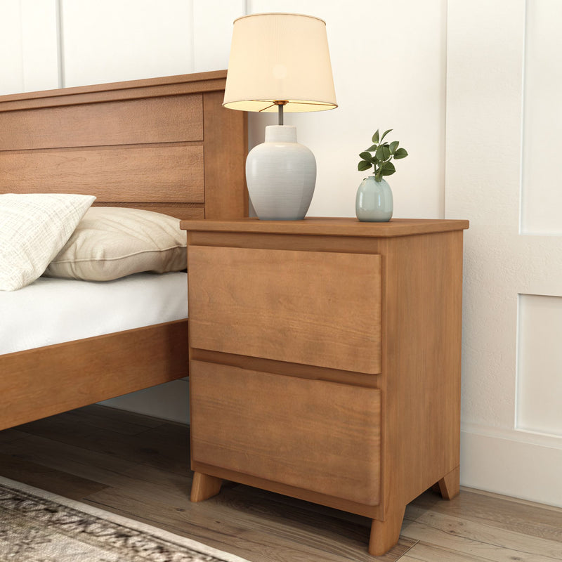 Wooden nightstand with two drawers beside a bed, featuring a white table lamp and a small plant for modern bedroom decor.