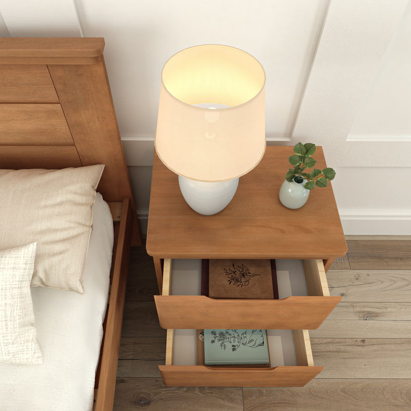 Wooden bedside table with a lamp and decorative plant, featuring open drawers containing books.