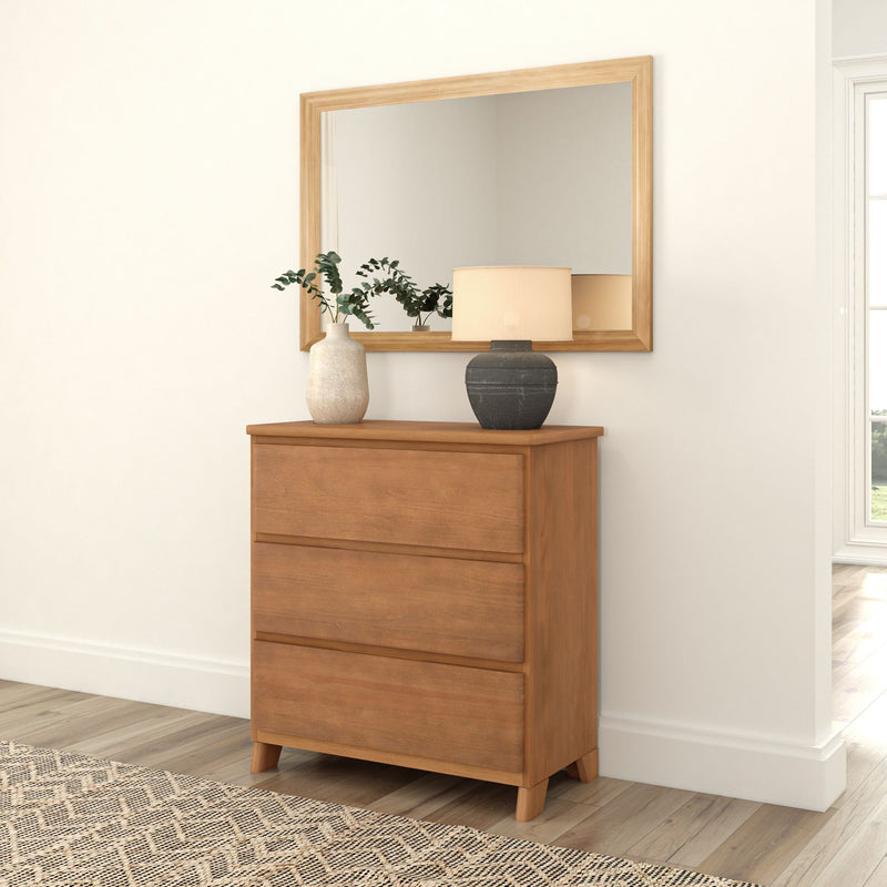 Wooden dresser with three drawers, topped with decorative vases and a lamp, placed beneath a matching framed mirror in a bright room with natural light.