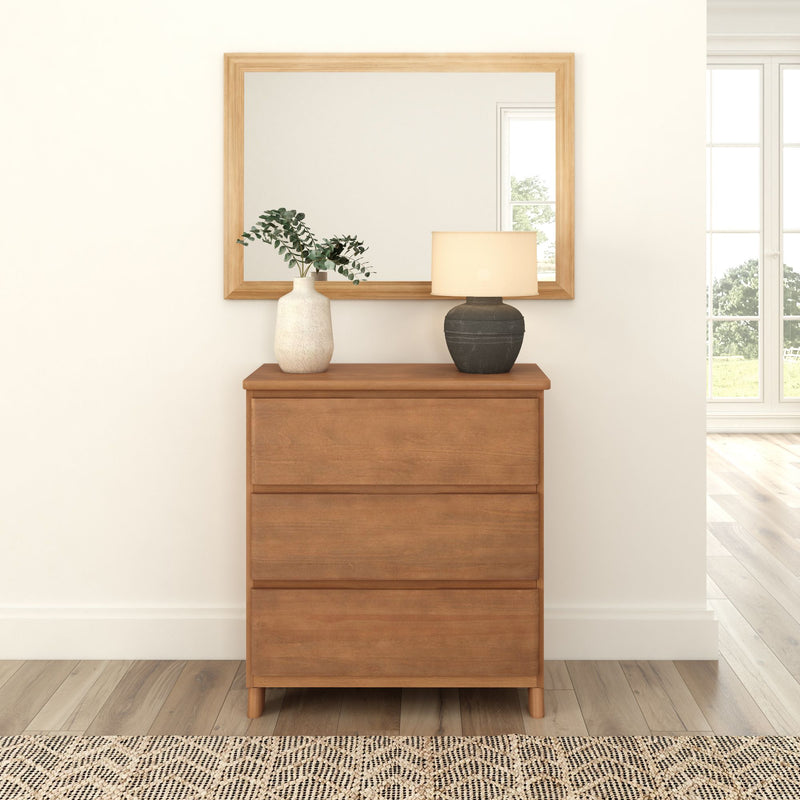 Wooden dresser with drawers, decorative vase, and lamp, complemented by a large mirror and natural light setting in a modern home interior.