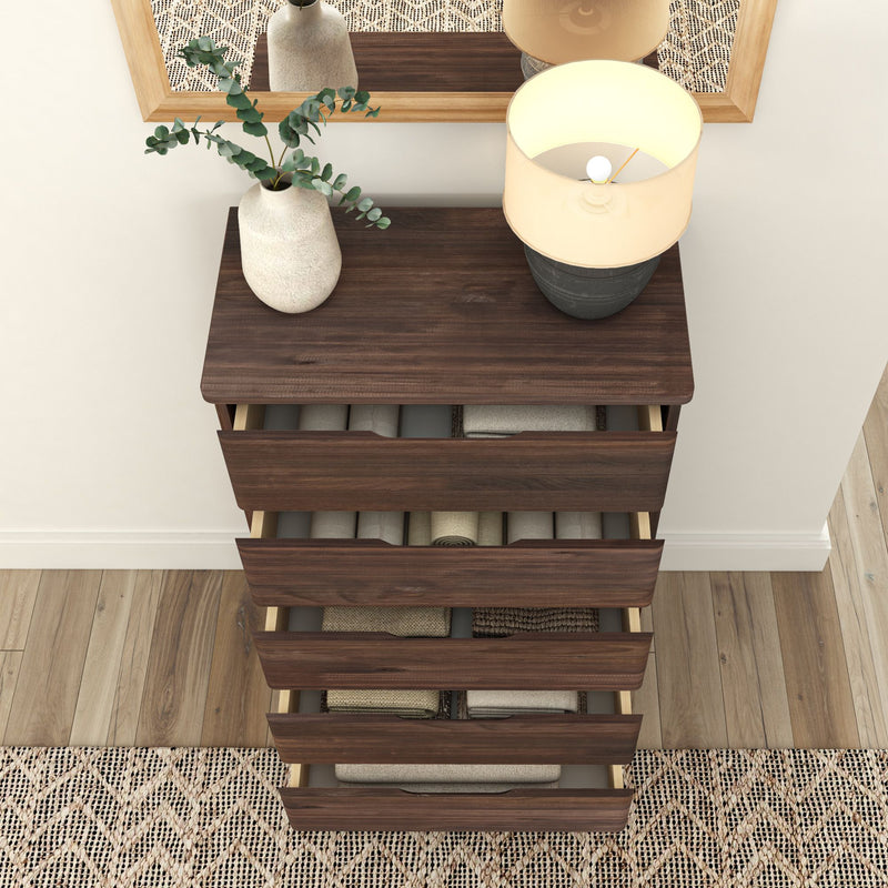 Dark wooden dresser with open drawers, showing neatly organized clothing, topped with a vase of greenery and a modern lamp, set against a decorative rug and wall mirror.