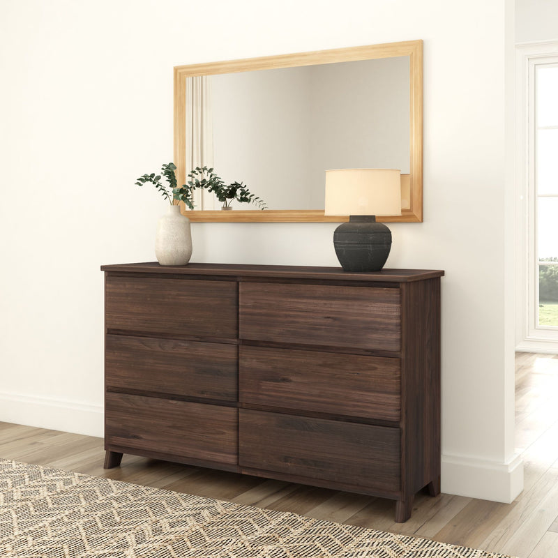 Dark wood dresser with six drawers, a decorative vase, and a lamp under a large mirror in a modern bedroom setting.