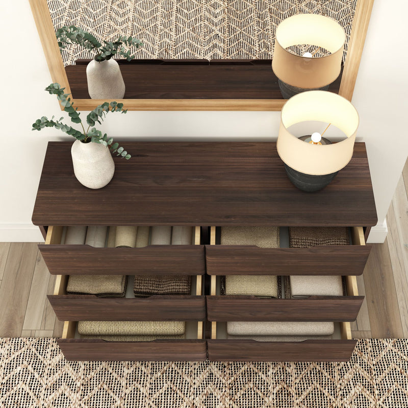 Modern six-drawer wooden dresser with decorative lamp and plant in a minimalist bedroom setting.