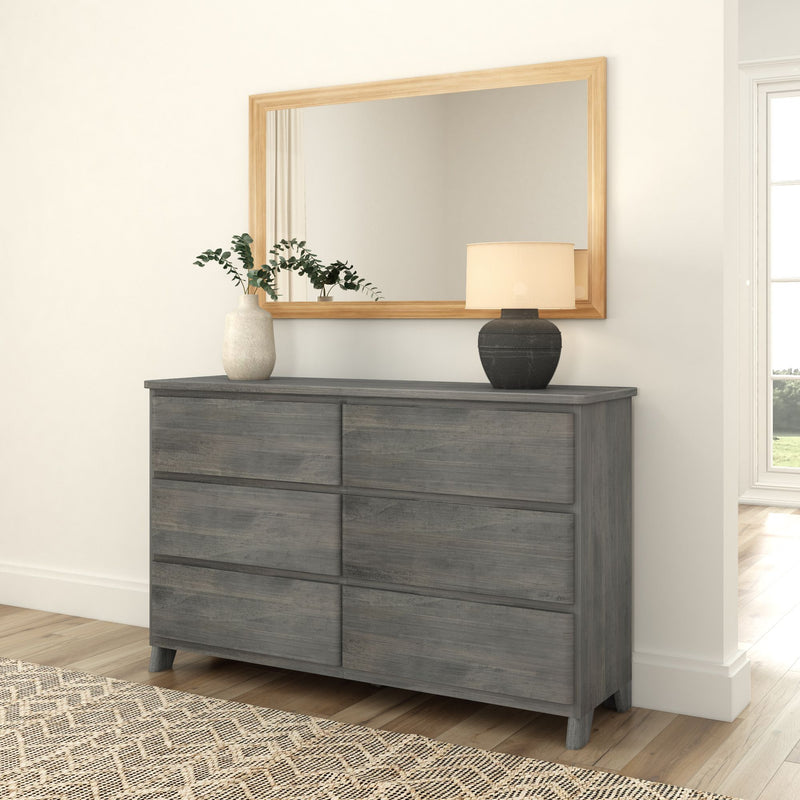Gray wooden dresser with decorative vase and lamp, in front of large wall mirror in bright minimalist bedroom.