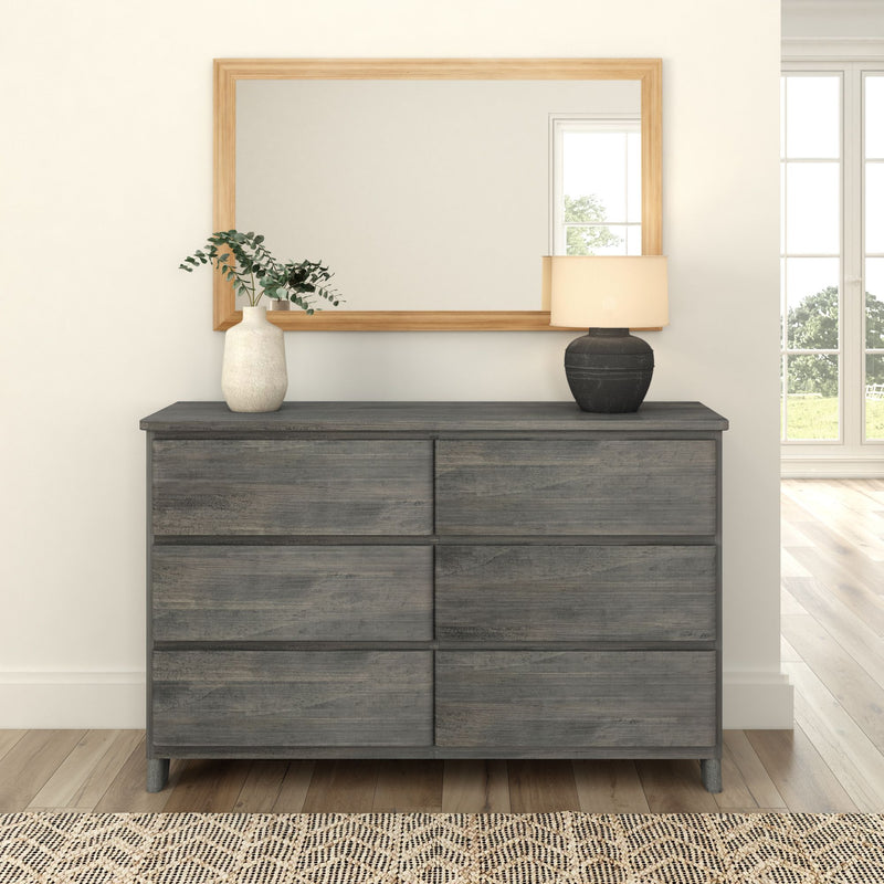 Gray wooden dresser with six drawers, topped with a white vase and a black lamp, in front of a large rectangular mirror.