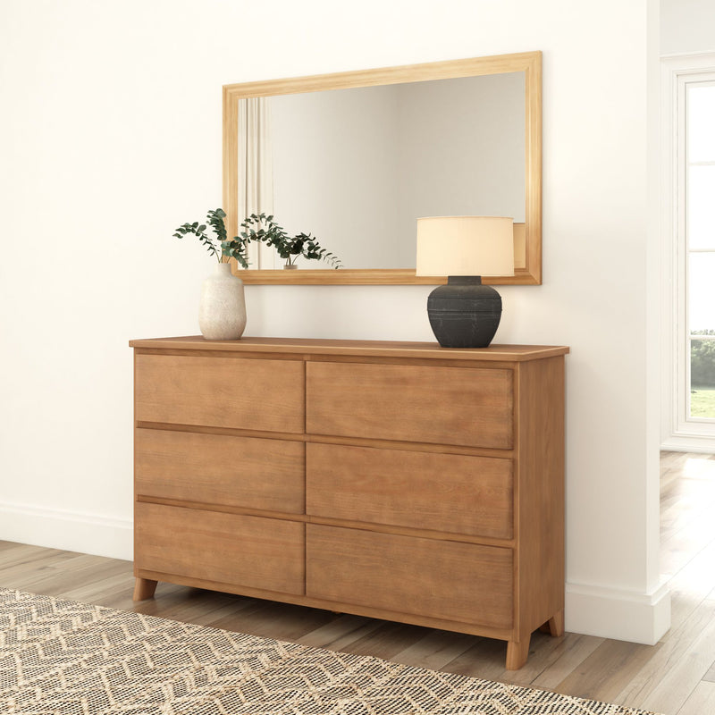 Wooden dresser with six drawers and decorative mirror, featuring a lamp and plant vase, in a modern bedroom setting.