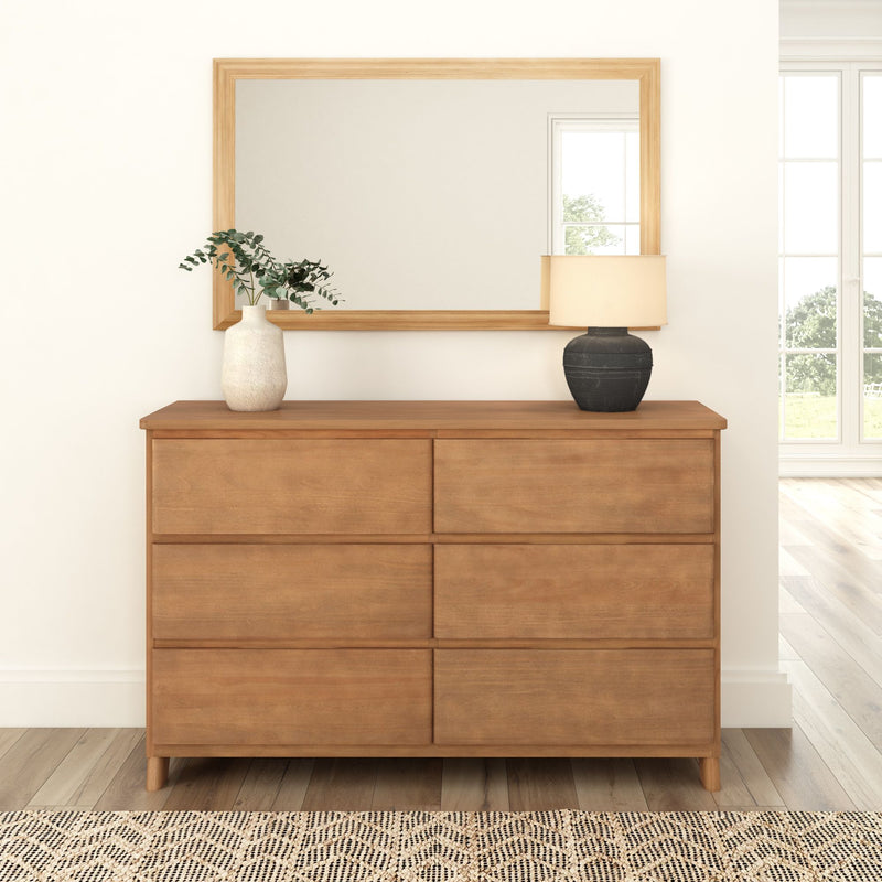 Modern wooden dresser with mirror, ceramic vase, and lamp in a stylish bedroom interior.