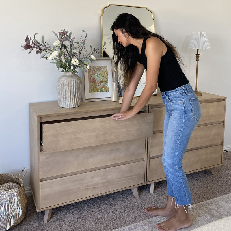 Woman opening drawer of modern mid-century wooden dresser in styled bedroom with decorative vase of flowers, mirror, lamp — home decor and storage solution