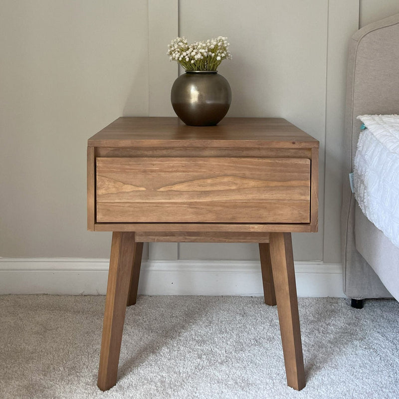 Mid-century modern wooden bedside table with a single drawer and a vase of white flowers placed on top.