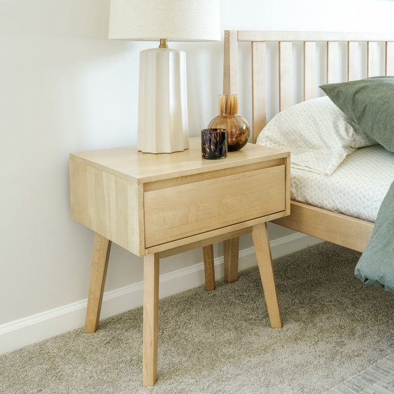 Mid-century modern wooden nightstand with decor and lamp in a cozy bedroom setting.