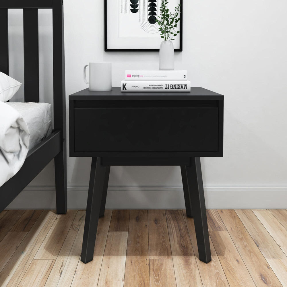 Modern black nightstand with drawer in minimalist bedroom decor.
