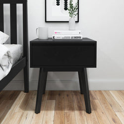 Modern black nightstand with drawer in minimalist bedroom decor.
