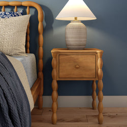 Wooden nightstand with textured ceramic table lamp, beige quilted pillows and spindle bed frame against a blue bedroom wall
