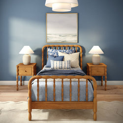 Coastal bedroom with wooden spindle bed, blue patterned bedding, two bedside lamps, wooden nightstands and framed ocean painting