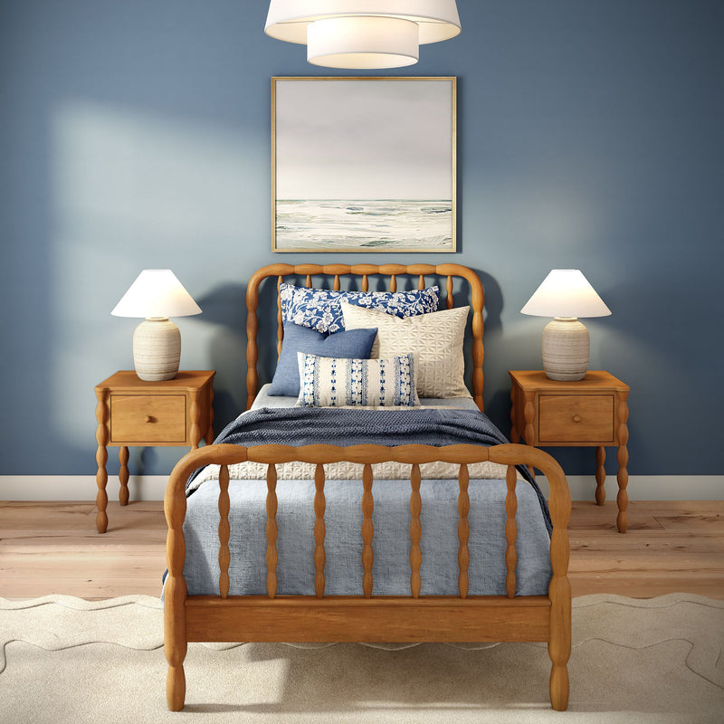 Coastal bedroom with wooden spindle bed, blue patterned bedding, two bedside lamps, wooden nightstands and framed ocean painting