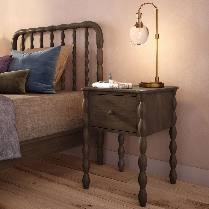 Cozy modern-rustic bedroom close-up showing dark wooden spindle headboard, wooden nightstand with brass table lamp, marble tray and velvet decorative pillows against a blush wall
