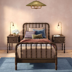 Cozy bedroom interior with dark wooden spindle bed, layered pillows and textured throw, brass bedside lamps, hydrangea bouquet on nightstand, pendant ceiling light and soft pastel pink walls
