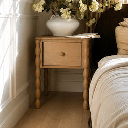 Wooden nightstand with turned legs, white ceramic vase of cream hydrangeas and open book in a neutral farmhouse bedroom