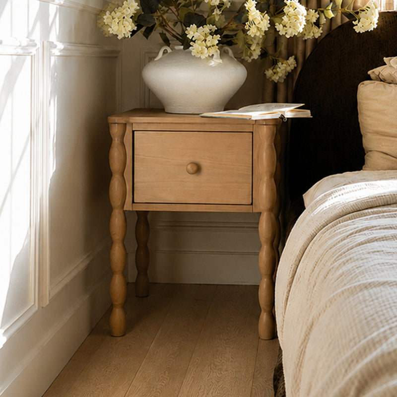 Wooden nightstand with turned legs, white ceramic vase of cream hydrangeas and open book in a neutral farmhouse bedroom