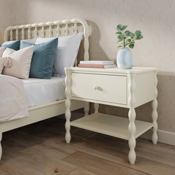Cream spindle bedside table with drawer and lower shelf beside matching spindle bed in farmhouse bedroom with teal pillows, eucalyptus vase and wood flooring