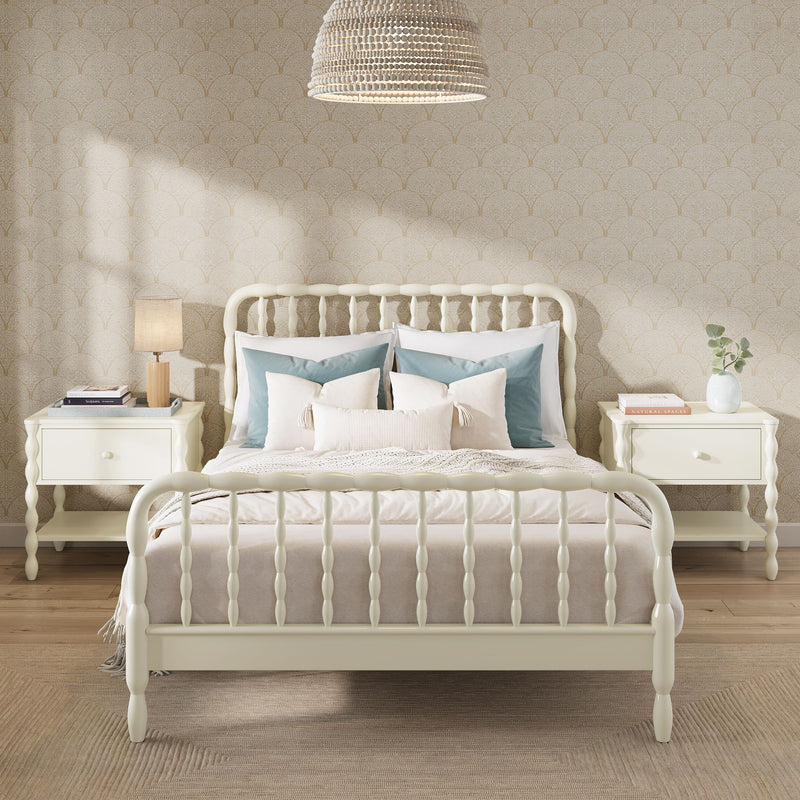 Cozy neutral farmhouse bedroom with cream spindle bed, layered beige and blue pillows, matching nightstands, table lamp, rattan pendant light and patterned wallpaper
