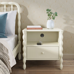 Cream bedside table nightstand with spindle legs, built-in charging outlet and drawer, styled with white vase and "Natural Spaces" book in bedroom