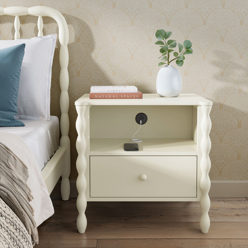 Cream bedside table nightstand with spindle legs, built-in charging outlet and drawer, styled with white vase and "Natural Spaces" book in bedroom