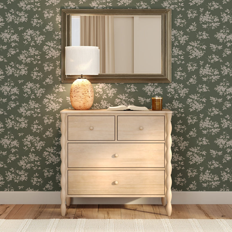 Light wood four-drawer dresser with ceramic table lamp and framed mirror against green floral wallpaper — cozy bedroom decor and rustic modern interior styling