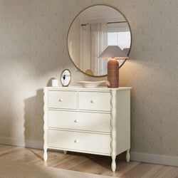 Cream four-drawer dresser with twisted legs topped by a round gold mirror, rattan table lamp and decorative bowl against beige patterned wallpaper on light wood floor