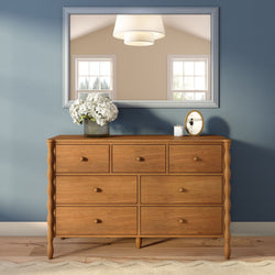 Natural wood chest of drawers against a blue accent wall with a large mirror, vase of white hydrangeas and candle — modern farmhouse bedroom dresser decor