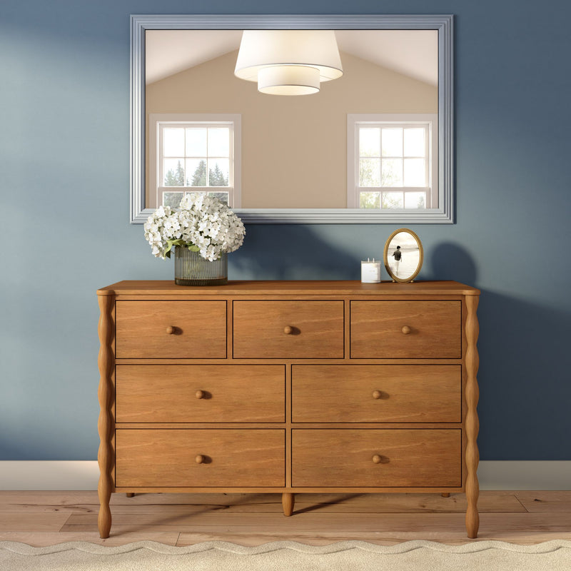 Natural wood chest of drawers against a blue accent wall with a large mirror, vase of white hydrangeas and candle — modern farmhouse bedroom dresser decor