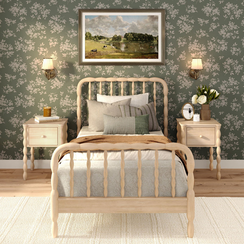 Cozy farmhouse bedroom with light wood spindle bed and matching nightstands, green floral wallpaper, neutral layered bedding, wall sconces and framed landscape artwork.